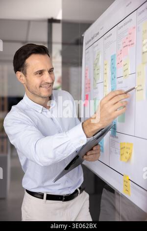 Smiling mid aged businessman add handwritten data on agile board Stock Photo