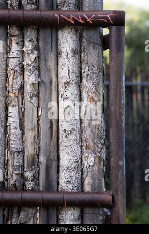 vertical of wood fence made from small tree trunks with textured bark held together with wire and metal piping urban nature grunge backdrop background Stock Photo