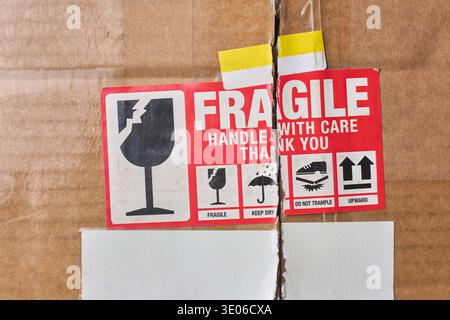 red fragile warning label and blank white stickers on brown cardboard box, printed black handling icons, top view closeup with copy space, shipping Stock Photo