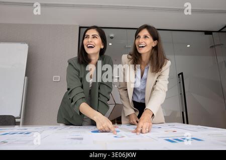 Happy women stand at table covered with charts and graphs Stock Photo