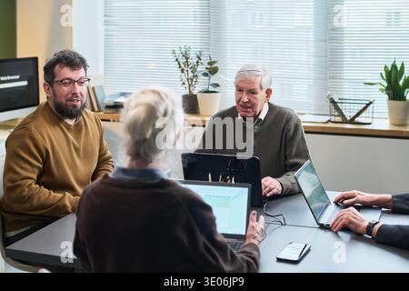 Group of senior Caucasian man, senior Caucasian woman, middle aged Caucasian man and middle aged Caucasian woman participating in computer literacy course using laptops and smartphones Stock Photo