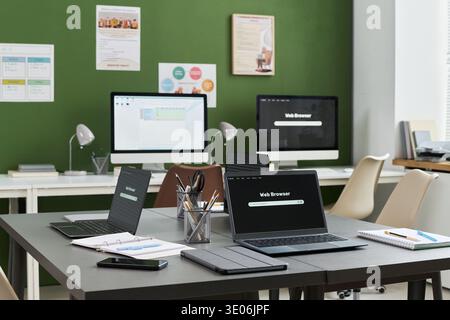 Empty classroom with multiple laptops, tablets, and desktop computers arranged on tables, digital devices displaying web browsers, educational materials suggesting computer literacy course setting Stock Photo