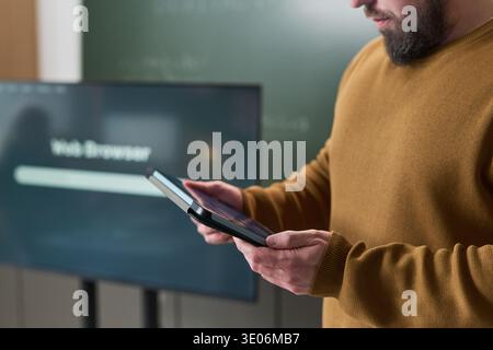 Midsection of man using digital tablet during computer literacy course standing in classroom with interactive display and chalkboard visible in background Stock Photo