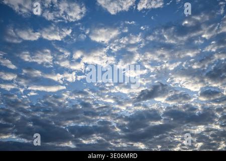 Dramatic blue sky with layers of scattered clouds and sunlight peeking through, creating a textured, peaceful atmosphere perfect for backgrounds, weat Stock Photo