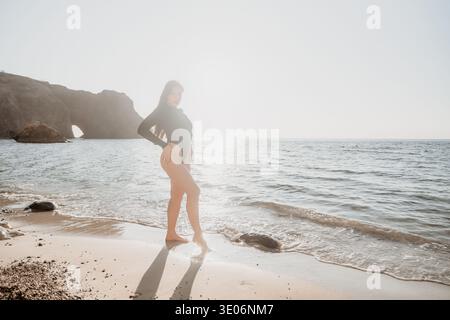 Woman beach bodysuit posing on a sandy shore with bright sunlight reflecting on the sea during a summer vacation Stock Photo