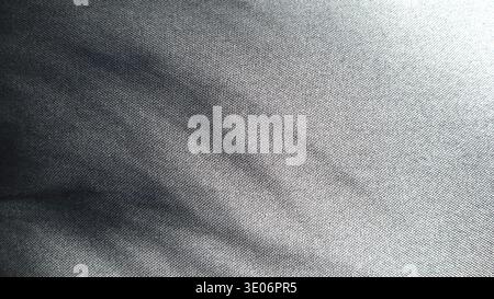 Photo of textured fabric of black color. From the upper left corner there is shadow from leaves of the plant. Thin long stripes. There is a light in the upper right corner. White gradient. Monochrome. Stock Photo