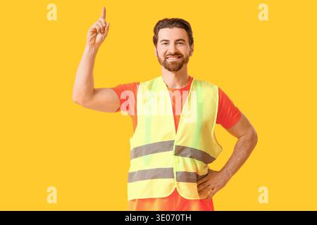 Young happy male construction worker in uniform pointing at something on yellow background Stock Photo