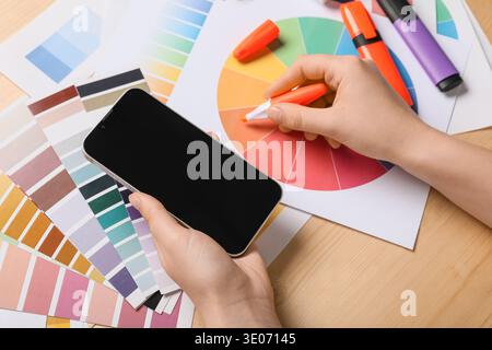 Female graphic designer with mobile phone, stationery and color palettes on brown wooden background, top view Stock Photo