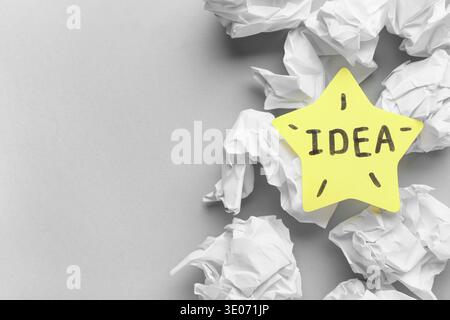 Sticky note with word IDEA and crumpled papers on grey background. Business idea concept Stock Photo