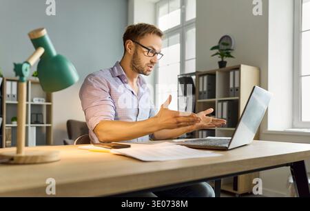 Frustrated man gesturing at laptop during remote troubleshooting in home office Stock Photo