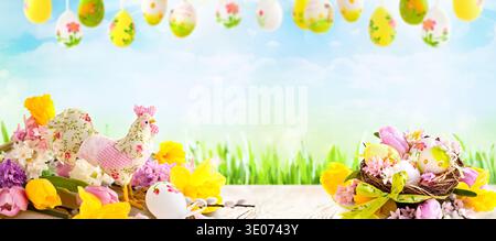 A table with a bunch of flowers and eggs on it. The table is surrounded by a blue sky and a green grassy field. The flowers and eggs are arranged in a Stock Photo