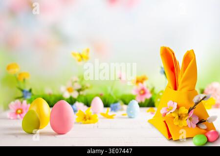 A table with a yellow napkin and three eggs on it. The napkin is folded into a bunny shape Stock Photo