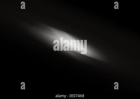 Soft light beam highlights a textured surface in a dark setting, creating a contrast between illuminated and shadowed areas, enhancing visual depth Stock Photo