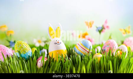 A bunny is standing in a field of Easter eggs. The eggs are scattered throughout the grass, with some being larger and others smaller. The bunny is th Stock Photo