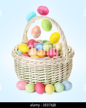 Color Easter eggs falling into basket on light blue gradient background Stock Photo