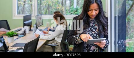 Banner of concentrated hispanic woman working with a tablet against an office window Stock Photo