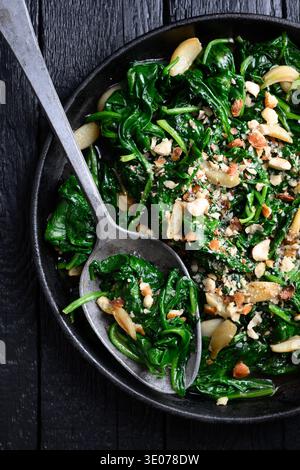 Flat lay of homemade sauteed spinach with garlic and nut topping in skillet. Natural ingredients, fresh cooking and balanced diet concept Stock Photo