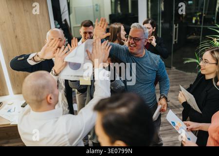 Team celebrates victory with high fives in a modern office after a successful project Stock Photo