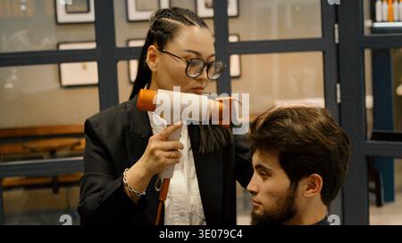 Female barber using a hair dryer for styling a client Stock Photo
