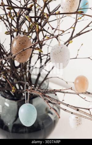 Easter tree decorated colorful pastel white and beige eggs. Birch branches with hang eggs in vase on white table. Vertical format. Spring greeting car Stock Photo