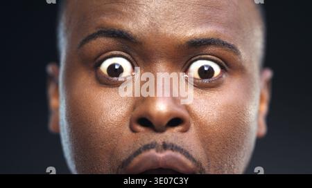 Portrait, reaction and surprise with black man in studio, facial expression and unexpected news. Big eyes, emoji and wow with African person in Stock Photo