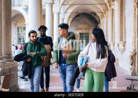 College campus life concept, diverse university students walking through a historic campus corridor between classes. Stock Photo