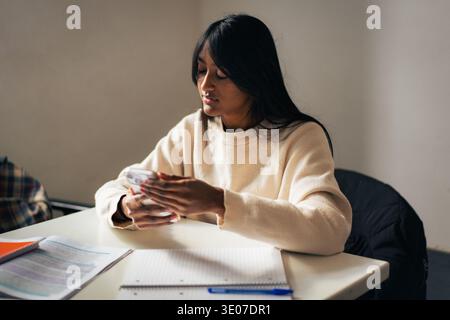 Digital student life concept, South Asian female university student using a smartphone at her classroom desk. Stock Photo