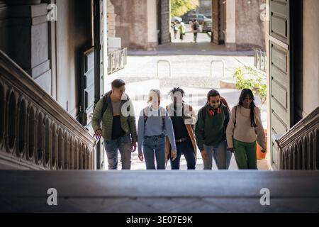College campus life concept, diverse university students walking up a historic staircase and talking between classes. Stock Photo