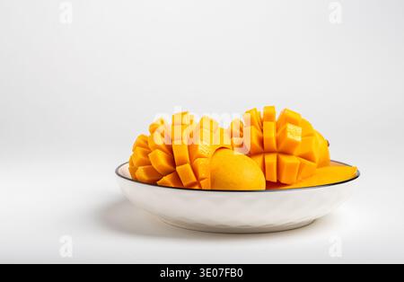 A bowl contains whole and diced mangoes isolated on white background Stock Photo