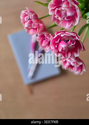 Cozy spring still life with pink tulips in a glass vase on a wooden table, morning coffee and soft natural light. Home lifestyle scene with flowers. Stock Photo
