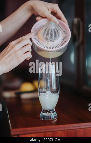 Woman squeezing lemon with manual juicer over a glass pouring fresh citrus juice Stock Photo