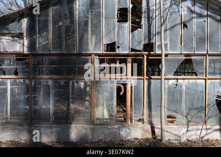 Abandoned greenhouse or industrial building with broken glass windows. Concept of decay, neglect, and ruined architecture.  Old ruined glass house in Stock Photo
