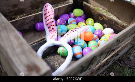 Bunny ears headband sitting on colorful plastic easter eggs in rustic wooden crate, ready for a hunt Stock Photo