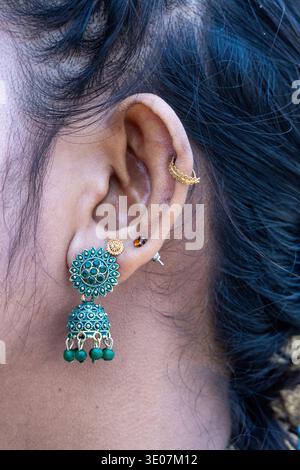 Close-up of a woman's ear featuring a traditional green Jhumka earring and elegant gold piercings. An exquisite South Asian fashion and ethnic jewelry Stock Photo