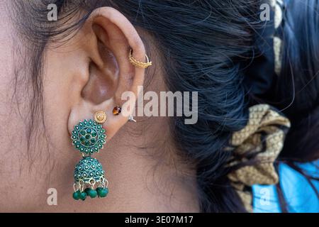Close-up of a woman's ear adorned with green Jhumka jewelry and gold piercings. A fusion of modern and traditional South Asian style, celebrating ethn Stock Photo