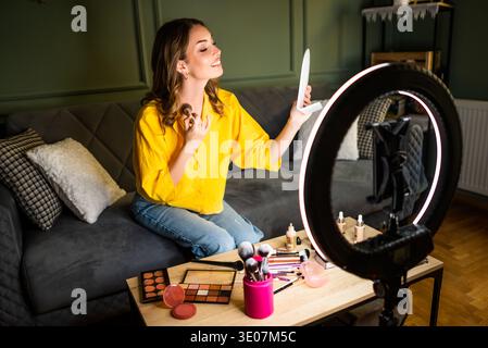 Influencer recording a beauty routine at home. She is using ring light and smartphone. Stock Photo