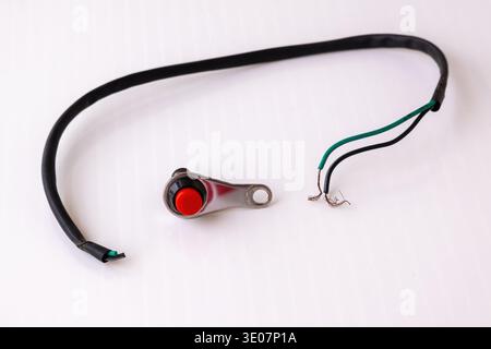 Close-up of a universal motorcycle handlebar push button switch with red button and electrical wiring on white background. Control switch for motorbik Stock Photo