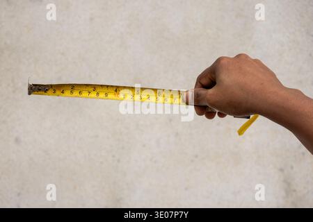 Close-up of a person hand holding and pulling a yellow measuring tape against a plain background. Concept of measurement, precision, construction, and Stock Photo