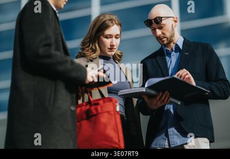 Multicultural business team meeting outdoors reviewing documents and discussing project details near office Stock Photo