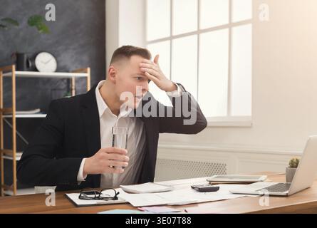 Stressed male manager working on laptop and drinking water Stock Photo