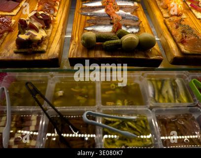 Selection of traditional Spanish tapas displayed on wooden boards inside a bar counter. Anchovies, salmon, tuna and various appetizers served Stock Photo