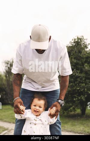 Portrait of cheerful baby girl with millennial father, warm candid family lifestyle. Cool Dad and child outdoors in park Stock Photo