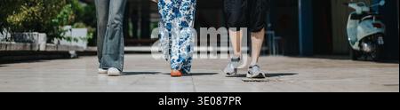 Three friends walk together on a sunny day, casual outfits, captured from a low-angle street scene Stock Photo