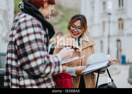 Two women outside, smiling, reviewing documents and discussing plans for a project together today Stock Photo