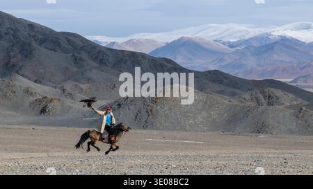 Mongolian eagle hunter (berkutchi) riding a horse with a blindfolded golden eagle, Altai Mountains, Bayan-Olgii, Western Mongolia, Mongolia Stock Photo