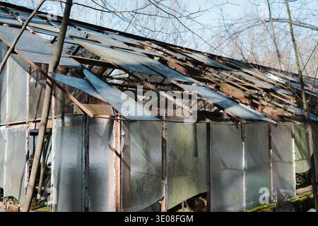 Broken glass roof of an abandoned greenhouse with shards hanging from rusty metal frames. Concept of danger, structural collapse, and neglect. Close-u Stock Photo