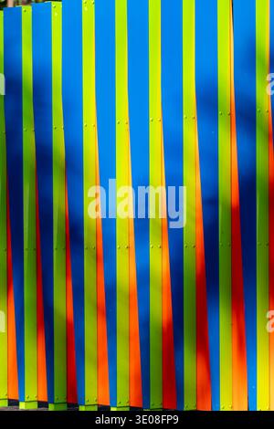 Modern architectural fence featuring vertical panels in striking blue, green, and orange, creating a dynamic abstract pattern and vibrant background. Stock Photo