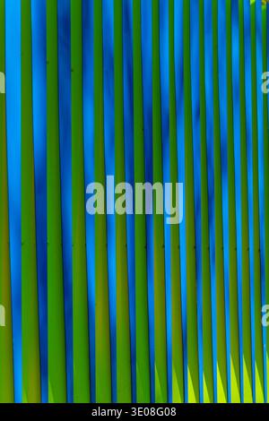 Bright blue and green vertical stripes form a modern metal fence, full-frame abstract background with geometric lines, vivid color contrast. Stock Photo