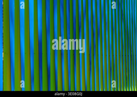 Green and blue vertical slats form a bold modern fence, repeating geometric stripes and shadows for vibrant graphic background - stock photo Stock Photo