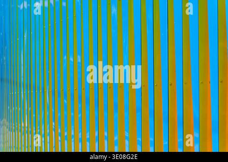 Modern fence featuring a pattern of alternating blue and yellow vertical metal panels creating a vibrant and engaging abstract background. Stock Photo